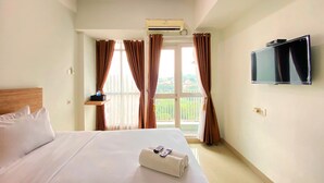 A hotel room with a bed, a TV mounted on the wall, and a window with curtains. - Warm And Cozy Studio At Taman Melati Jatinangor Apartment (Hegarmanah)
