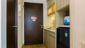 A narrow hallway with a wooden door, a built-in sink, and a black refrigerator with a green sticker. - Minimalist And Warm Studio At Transpark Bintaro Apartment (South Tangerang)