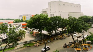 A modern building with a flat roof and large windows, surrounded by trees and parked vehicles. - Minimalist And Warm Studio At Transpark Bintaro Apartment (South Tangerang)