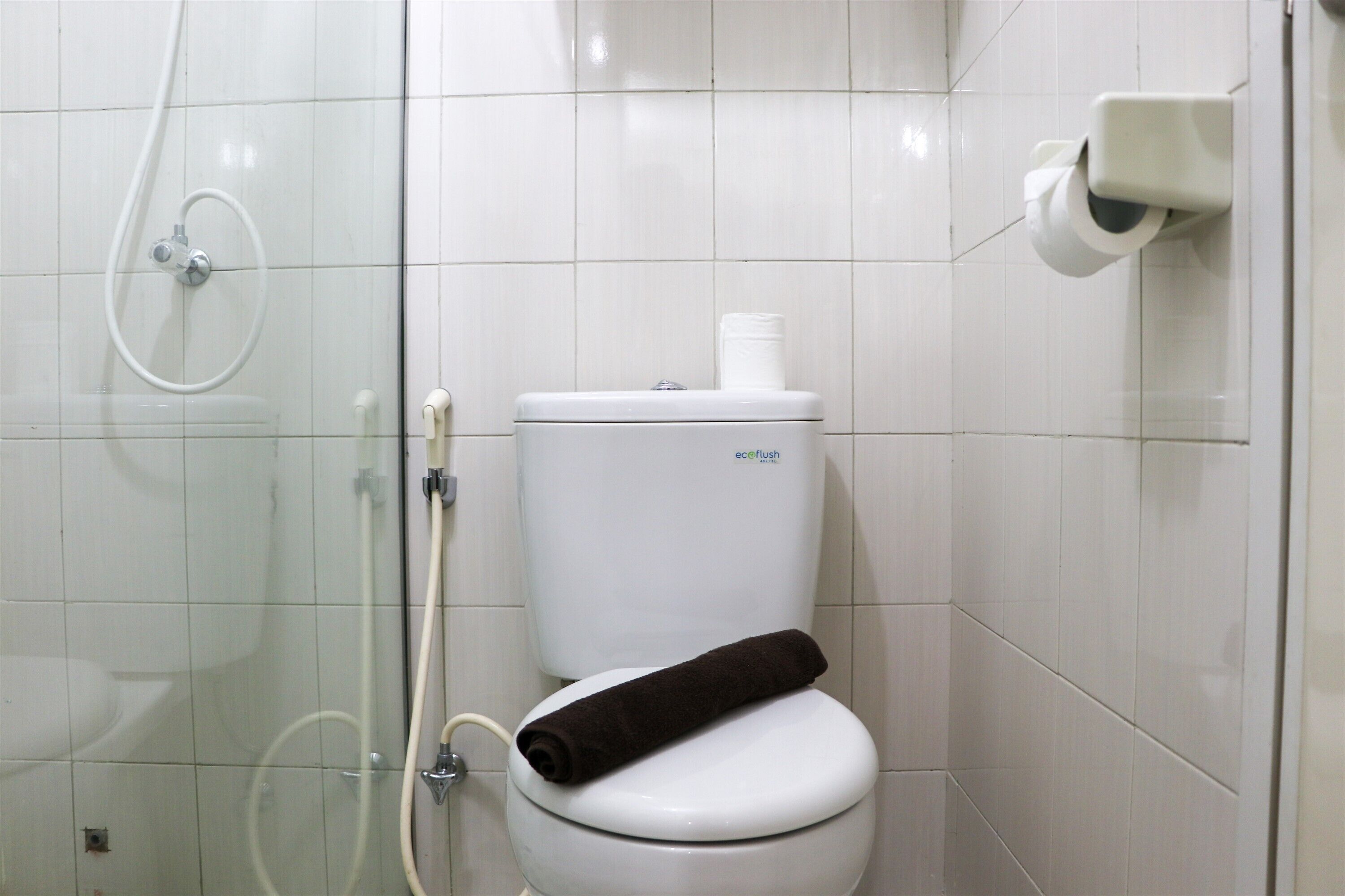 A white toilet with a black towel on the seat, a glass shower enclosure, and a toilet paper holder on the wall.
