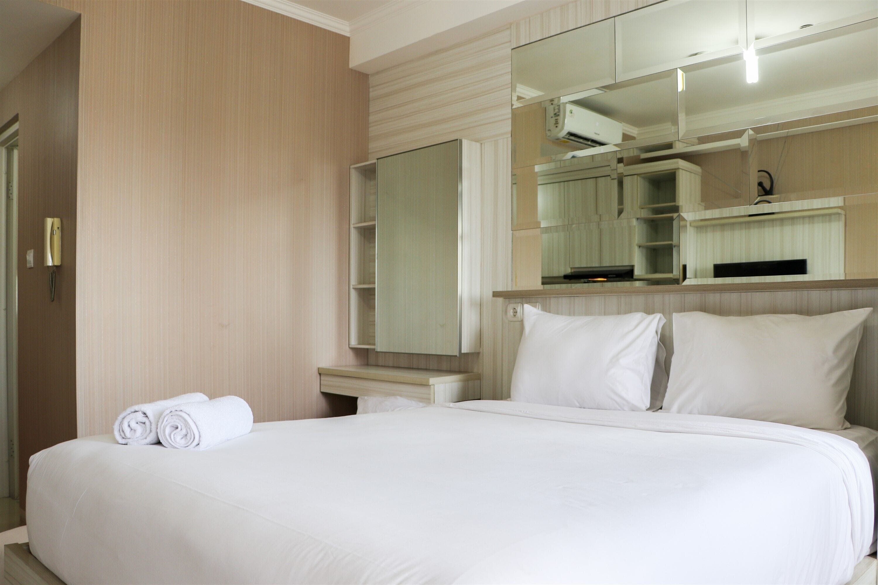 Quarto de hotel com uma cama grande, guarda-roupa embutido, espelho e mesa de cabeceira pequena.