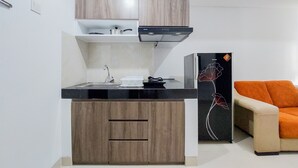 A compact kitchen with wooden cabinets, a black countertop, and a modern stove. - Luxurious 2Br At Serpong Garden Apartment (Cisauk)
