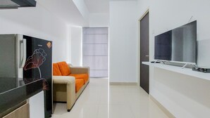 A modern living room with a flat-screen TV, a sofa with orange cushions, and a black cabinet with a floral design. - Luxurious 2Br At Serpong Garden Apartment (Cisauk)