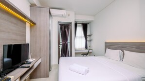 A modern hotel room with a flat-screen TV, a desk with a computer, a bed with white linens, and a window with curtains.
