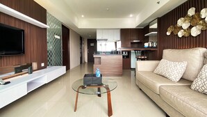A modern living room with a sofa, coffee table, TV, and kitchen in the background. - Luxury 2Br Apartment At Tamansari La Grande (Bandung)