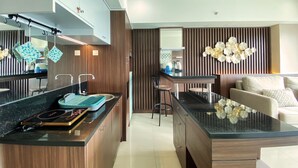 A modern kitchen with a central island, wooden cabinets, and a dining area with a sofa. - Luxury 2Br Apartment At Tamansari La Grande (Bandung)