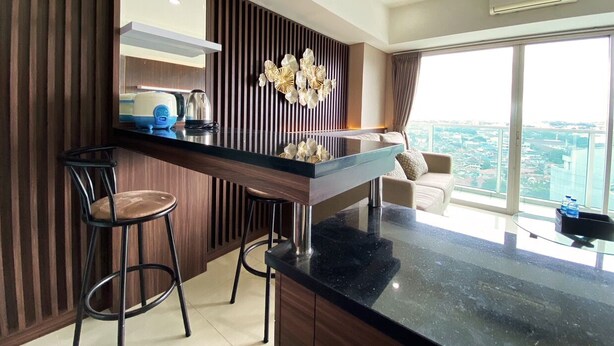 A modern kitchen with a central island, bar stools, and a view of the city through large windows. - Luxury 2Br Apartment At Tamansari La Grande (Bandung)