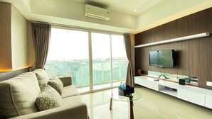 A modern living room with a sofa, a coffee table, a flat-screen TV, and a large window with curtains. - Luxury 2Br Apartment At Tamansari La Grande (Bandung)