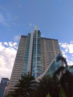 A tall, modern skyscraper with a distinctive central tower and multiple balconies. - Comfort And Modern Look Studio Apartment At Ambassade Kuningan (Jakarta)