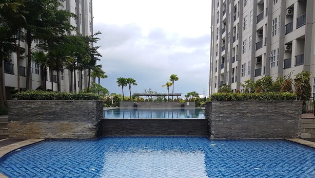 A swimming pool with a tiled floor, surrounded by a stone wall and palm trees. - Pleasurable 1Br Apartment At Saveria Bsd City (Pagedangan)