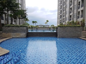 A swimming pool with a tiled floor, surrounded by a stone wall and greenery.