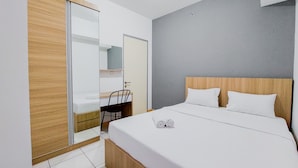 A modern hotel room with a wooden headboard, a large bed with white linens, a desk with a chair, and a sliding door closet. - Nice Designed And Comfort 2Br Apartment At M-Town Residence (Gading Serpong)