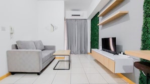 A modern living room with a grey sofa, a wooden coffee table, a TV on a wooden stand, and a green wall accent. - Nice Designed And Comfort 2Br Apartment At M-Town Residence (Gading Serpong)