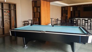 A pool table in a modern room with a bar area and seating. - Cozy And Well Furnished 2Br At Branz Bsd City Apartment (Pagedangan)