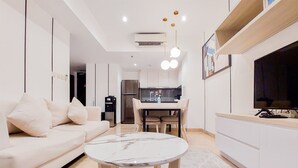A modern living room with a white sofa, a marble coffee table, and a dining area with a kitchen in the background. - Cozy And Well Furnished 2Br At Branz Bsd City Apartment (Pagedangan)