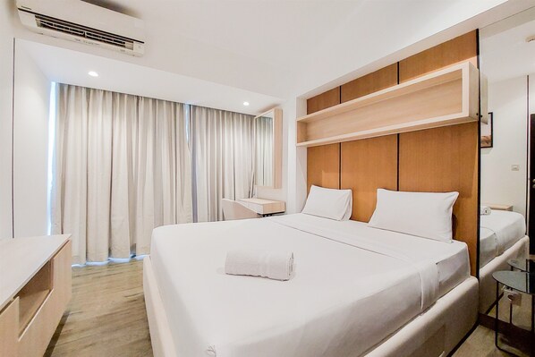 A hotel room with a large bed, a desk, a chair, and a window with curtains.