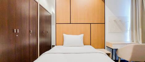 A hotel room with a bed, a desk, and a chair. There are wooden wardrobes and a wall-mounted pegboard.