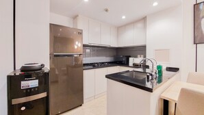 A modern kitchen with white cabinets, a stainless steel refrigerator, a built-in microwave, and a sink with a black countertop. - Cozy And Well Furnished 2Br At Branz Bsd City Apartment (Pagedangan)