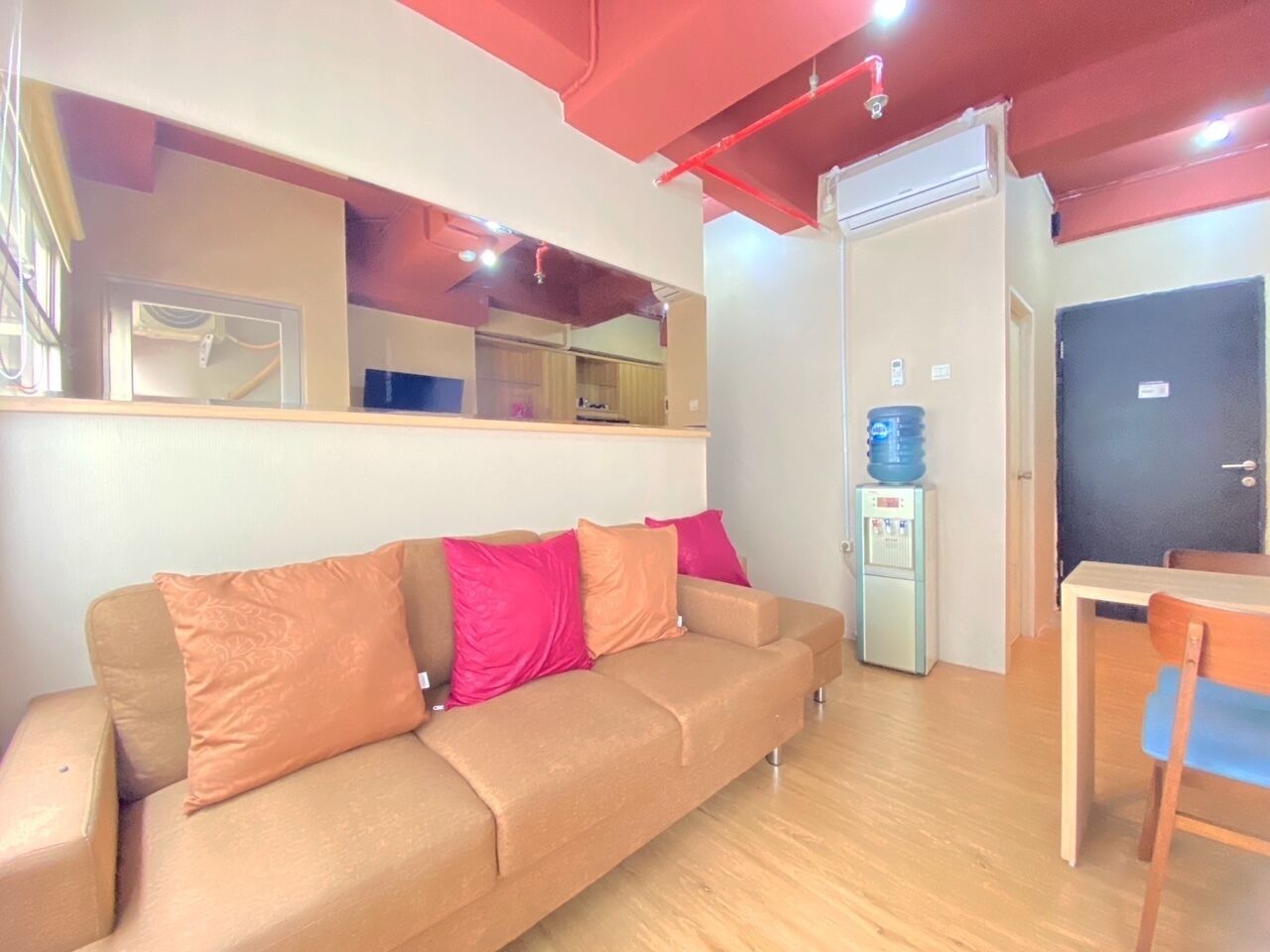 Una habitació amb un sofà beix, un dispensador d'aigua, una taula petita i una porta.