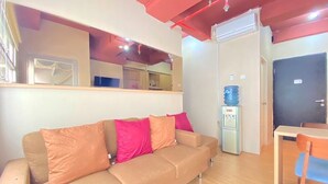 Una habitación con un sofá color beige, un dispensador de agua, una mesita y una puerta.