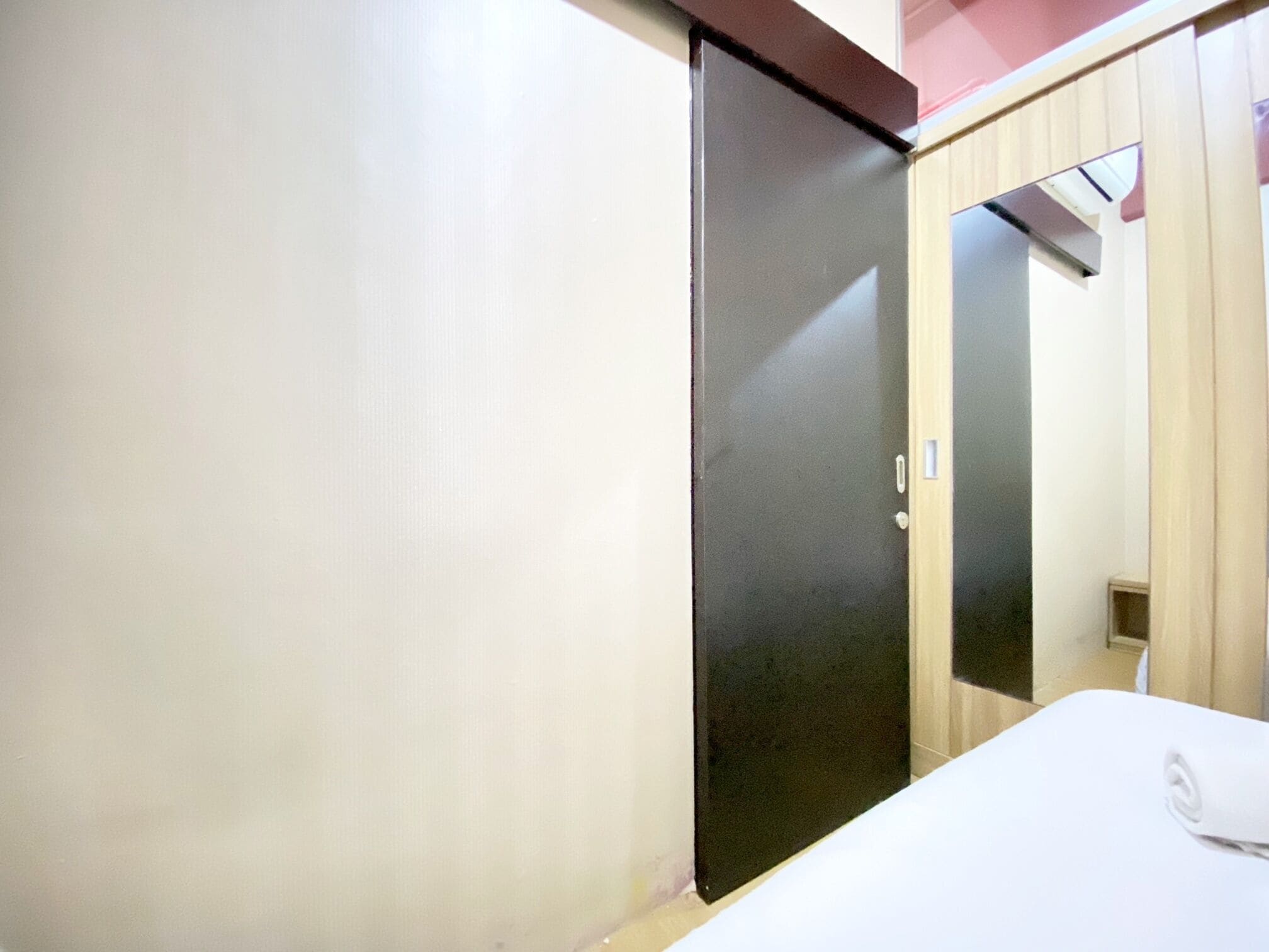 Habitació amb un llit blanc, una porta corredissa fosca i un armari de fusta.