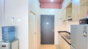 Un pasillo estrecho con un dispensador de agua a la izquierda, una puerta al final y una zona de cocina a la derecha.