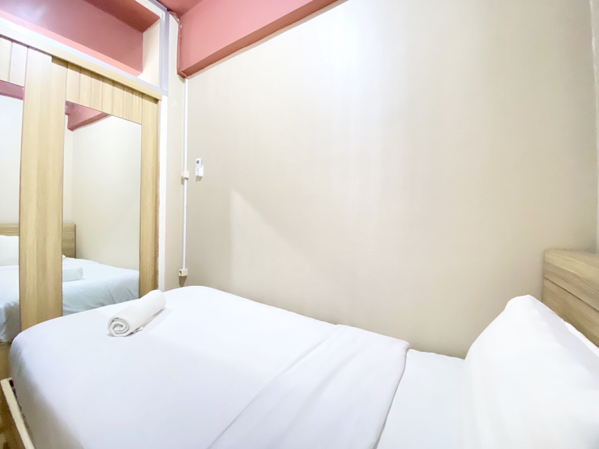 A single bed with a white mattress and pillows, a wooden headboard, and a wooden nightstand with a lamp.