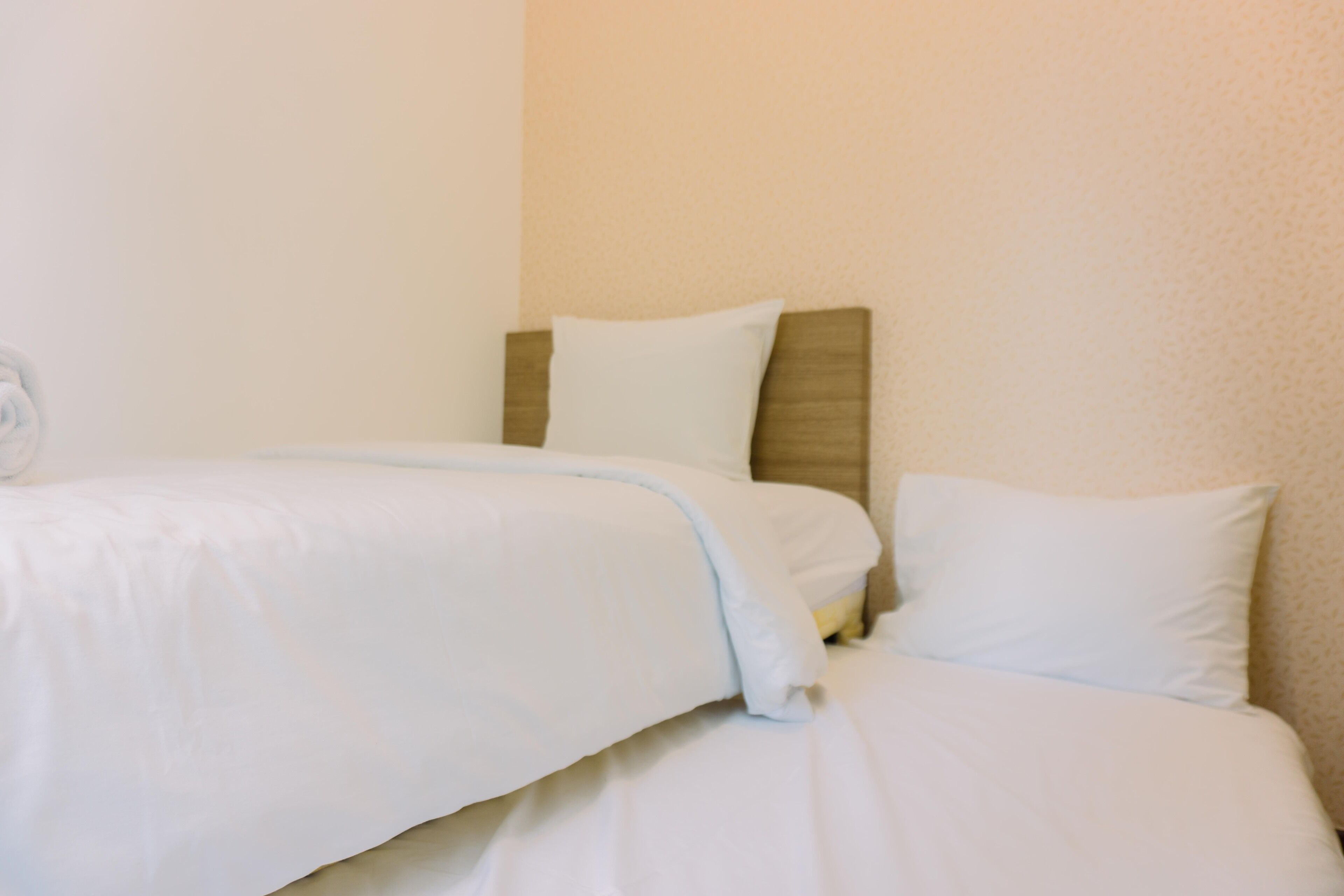 A neatly made bed with white bedding and a wooden headboard.