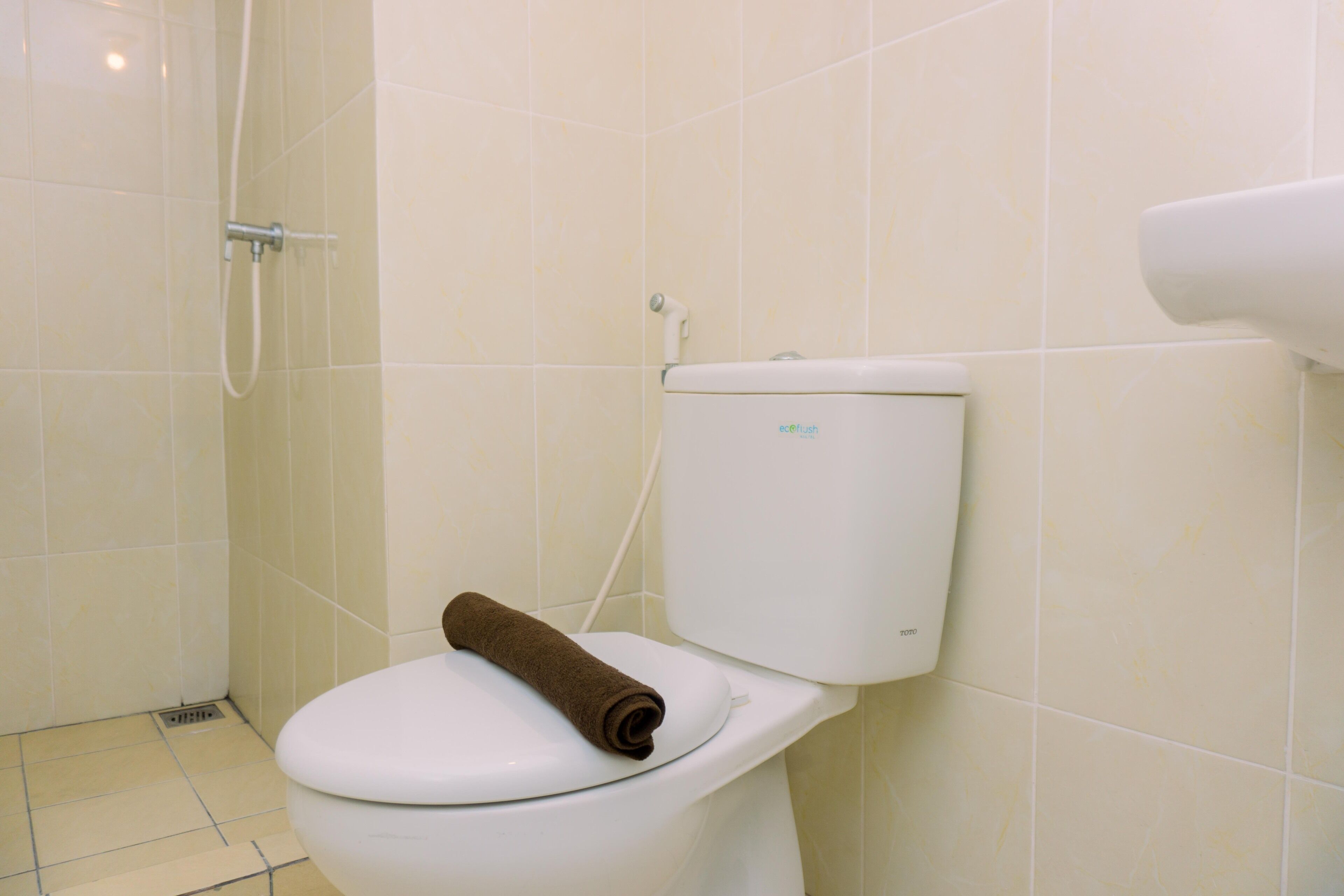 A toilet with a brown towel on the seat, a white flush handle, and a white flush button on the tank.