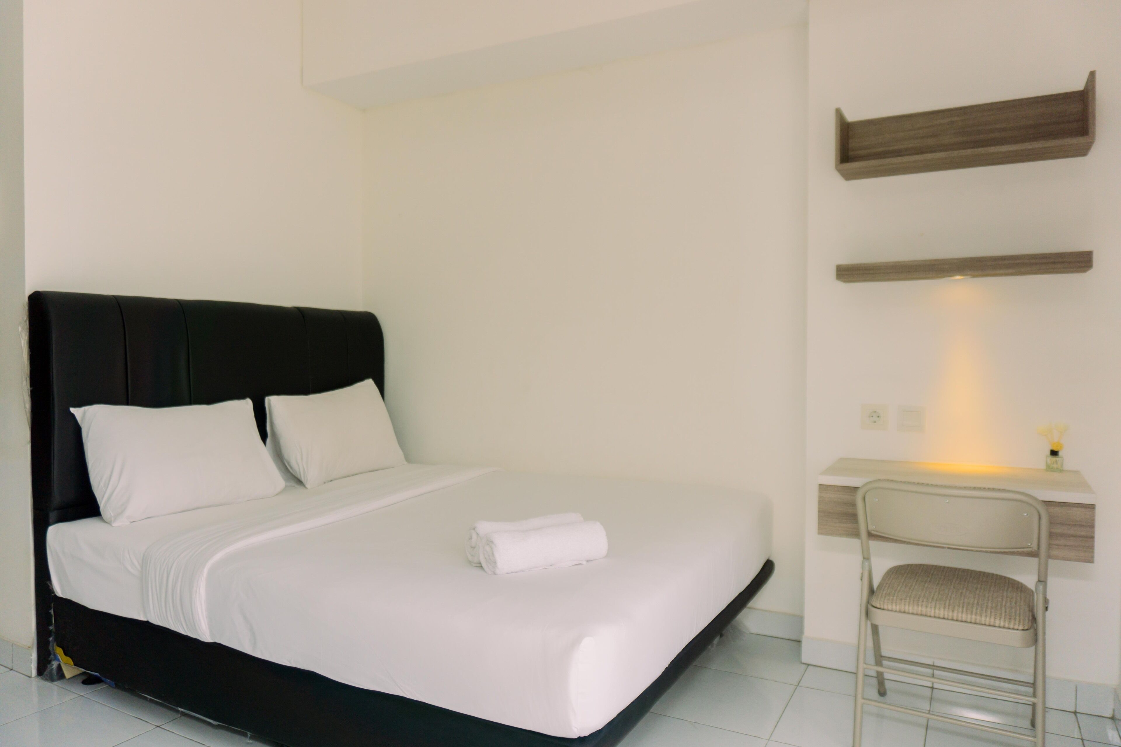 Una cama bien hecha con ropa de cama blanca, un cabecero negro y una toalla doblada sobre la cama.