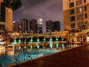 A nighttime swimming pool with a city skyline in the background. - Stunning And Comfortable 3Br Apartment Casa Grande Residence (Jakarta)
