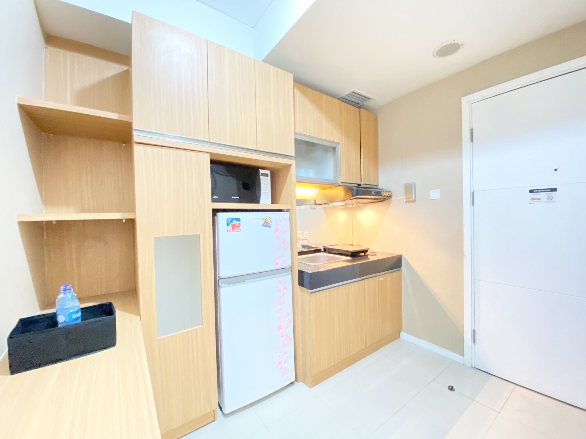 A compact kitchen with wooden cabinets, a refrigerator, a microwave, and a sink.