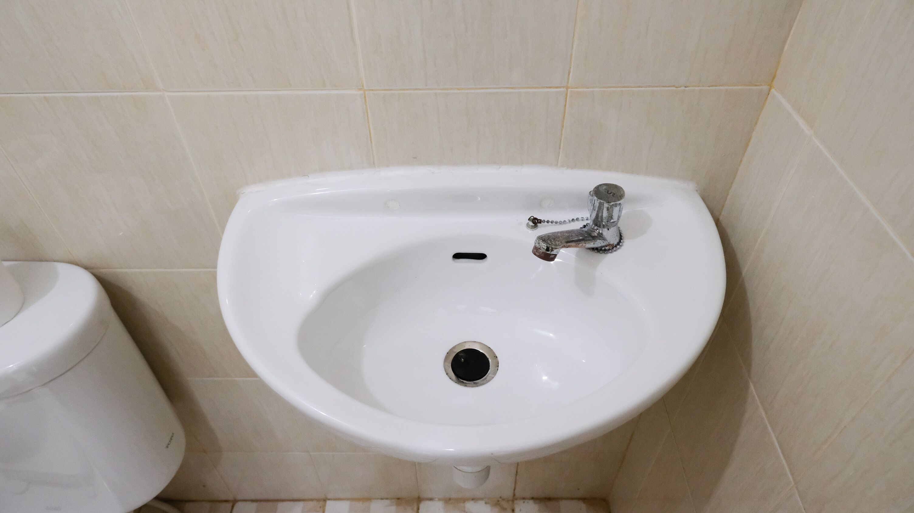 A white bathroom sink with a chrome faucet, a small drain hole, and a toilet to its left.