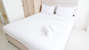Un lit bien fait, avec du linge de lit blanc et deux serviettes enroulées.