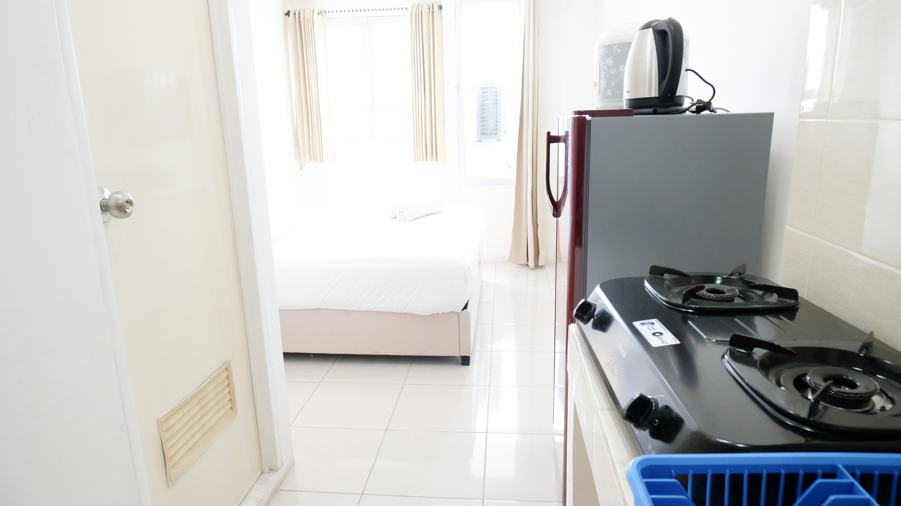 Hotellihuone, jossa on sänky, pieni keittiönurkkaus kaasuliedellä sekä sininen pyykkikori.