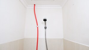 Une douche avec un tuyau rouge et un pommeau de douche portatif.