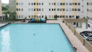 En swimmingpool med en vattenrutschkana och en lekplats för barn, omgiven av en flervåningsbyggnad med balkonger.