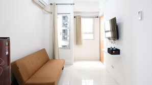 Ett hotellrum med en soffa, en TV som är monterad på väggen, en minibar och ett fönster med gardiner.