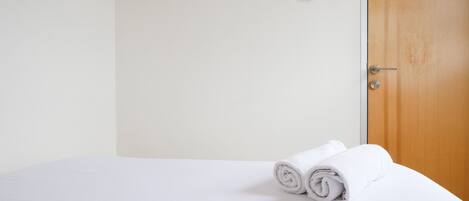 A neatly made bed with rolled white towels, a wooden door, and a wall-mounted thermostat.