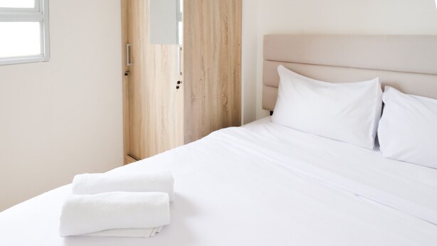 Een net opgemaakt bed met witte lakens en kussens, een houten deur en een witte muur.