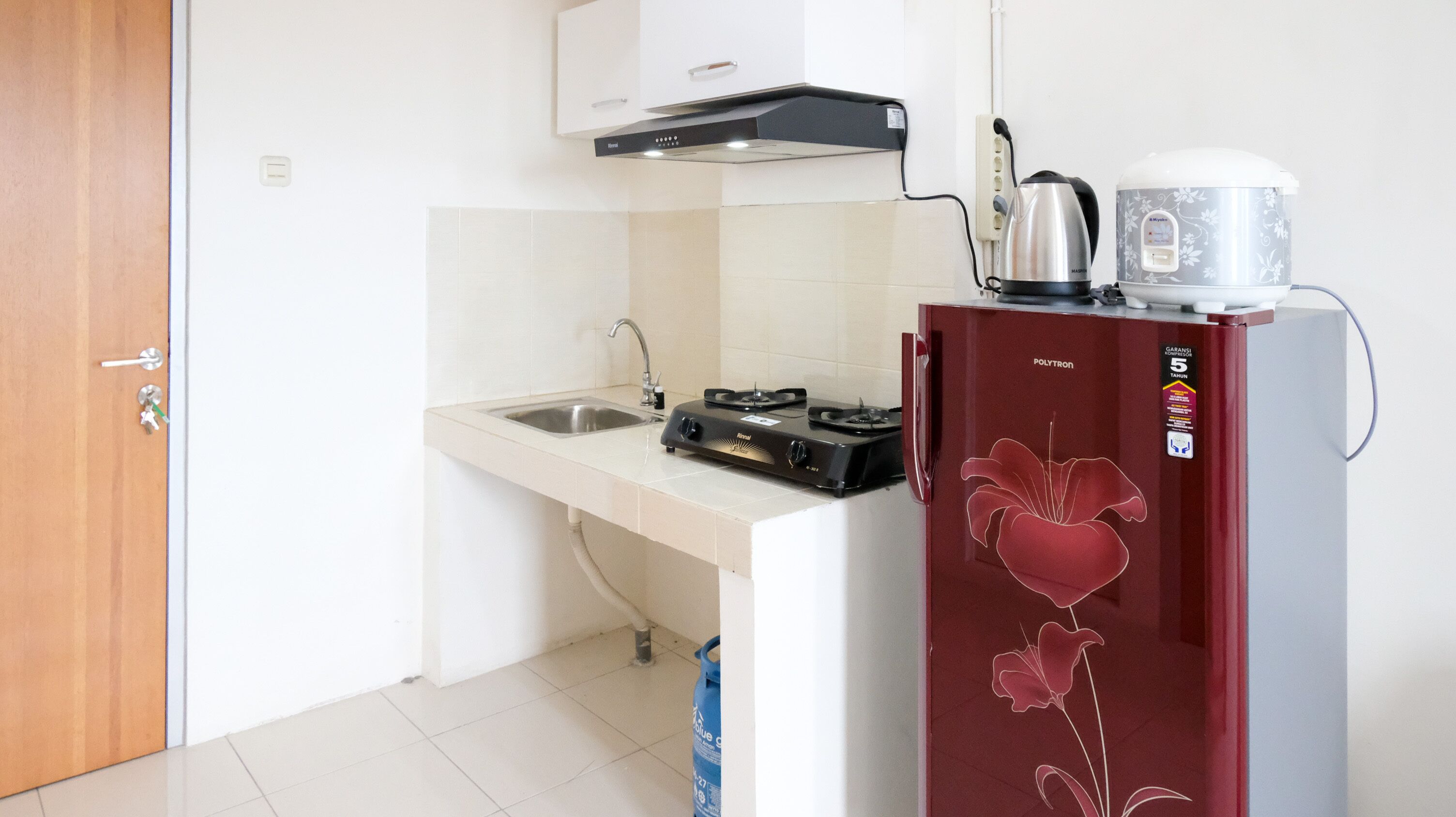 A compact kitchen with a gas stove, a kettle, and a refrigerator.
