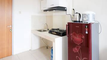 A compact kitchen with a gas stove, a kettle, and a refrigerator.