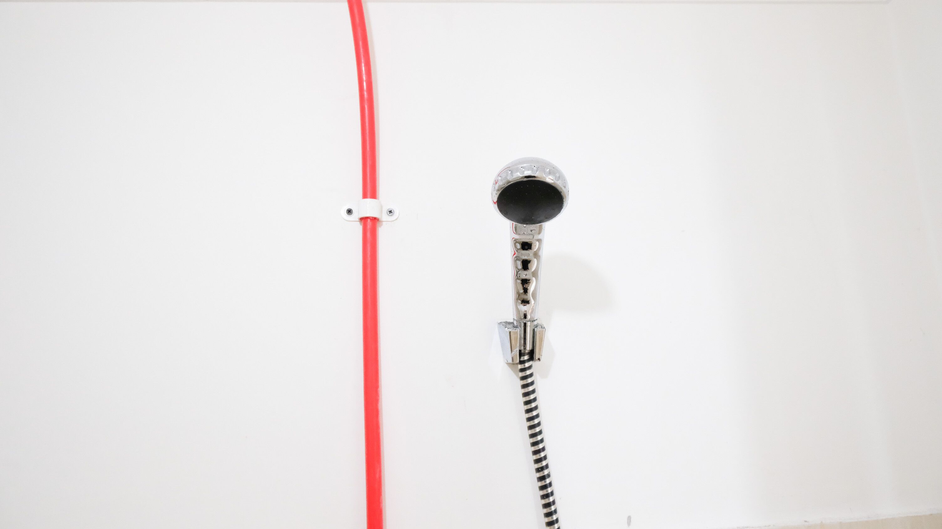 A metallic hairdryer mounted on a white wall with a red hose attached.