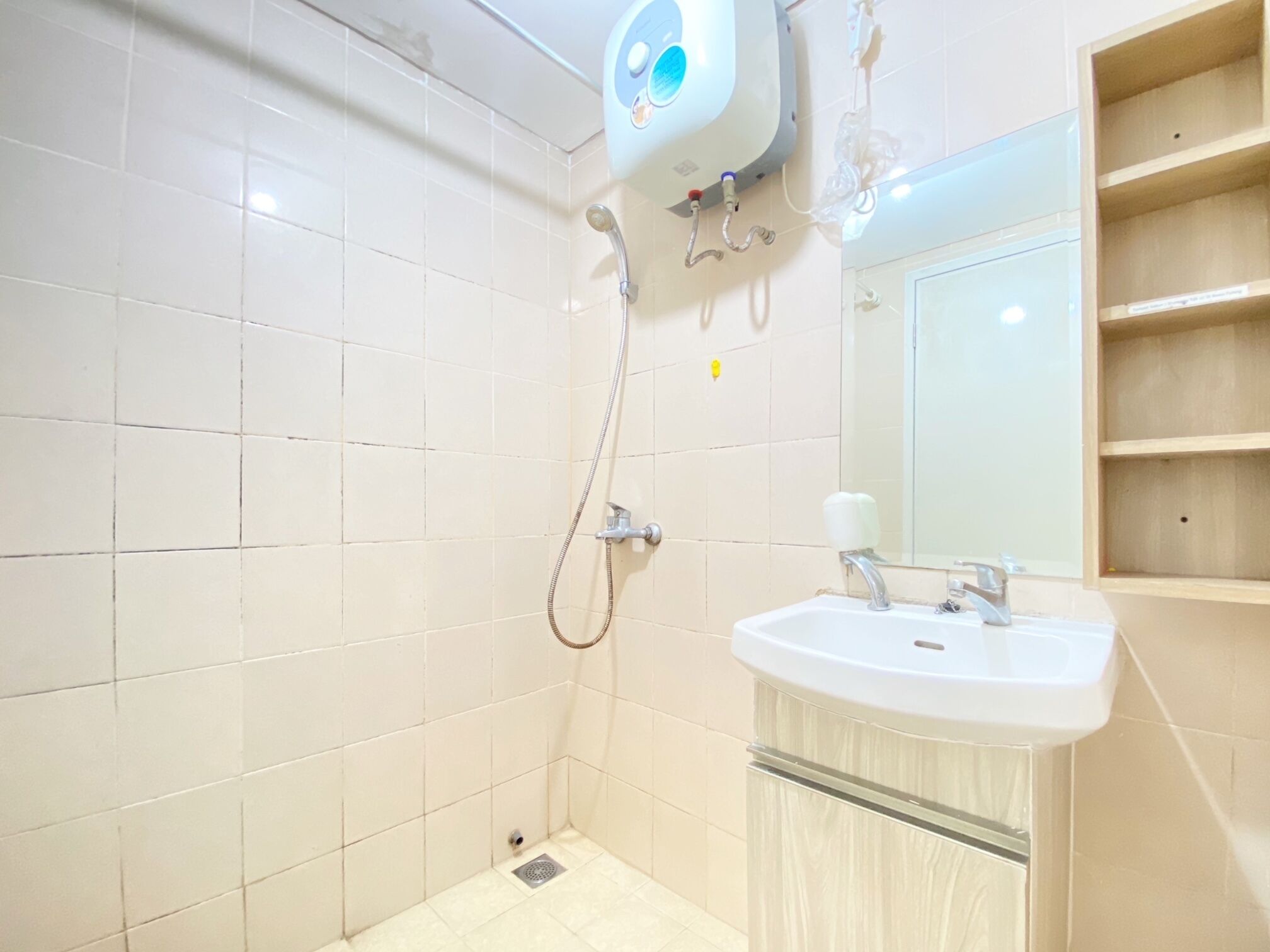 Un baño con azulejos blancos, ducha con cabezal de ducha manual, lavamanos con espejo y retrete.