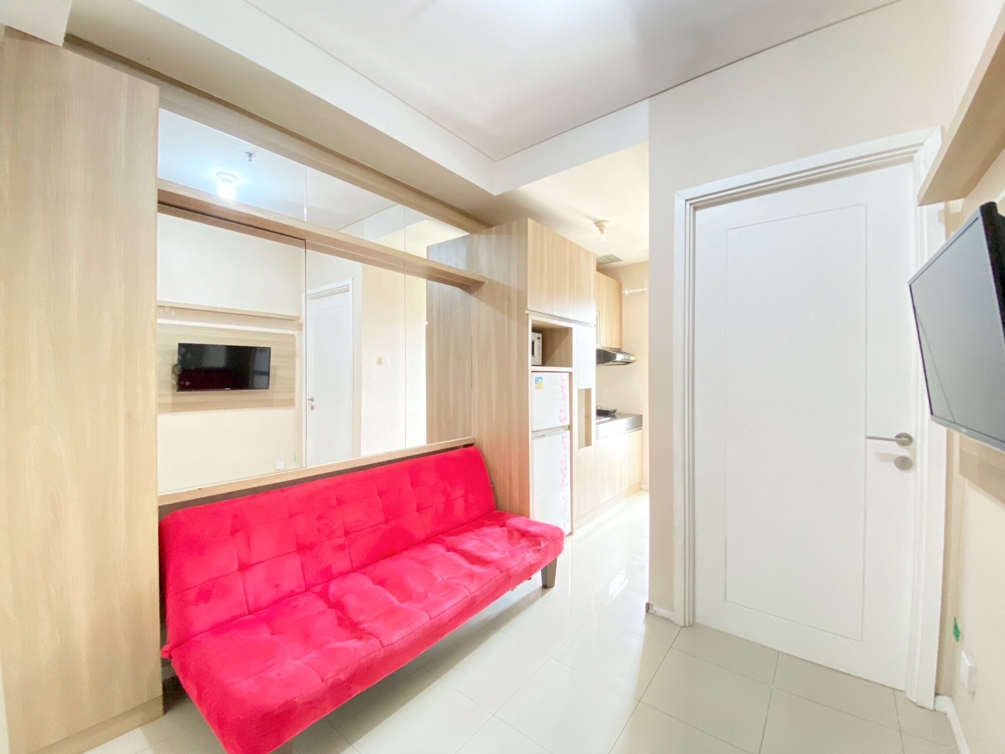 A hallway with a red sofa, a white door, and a TV mounted on the wall.
