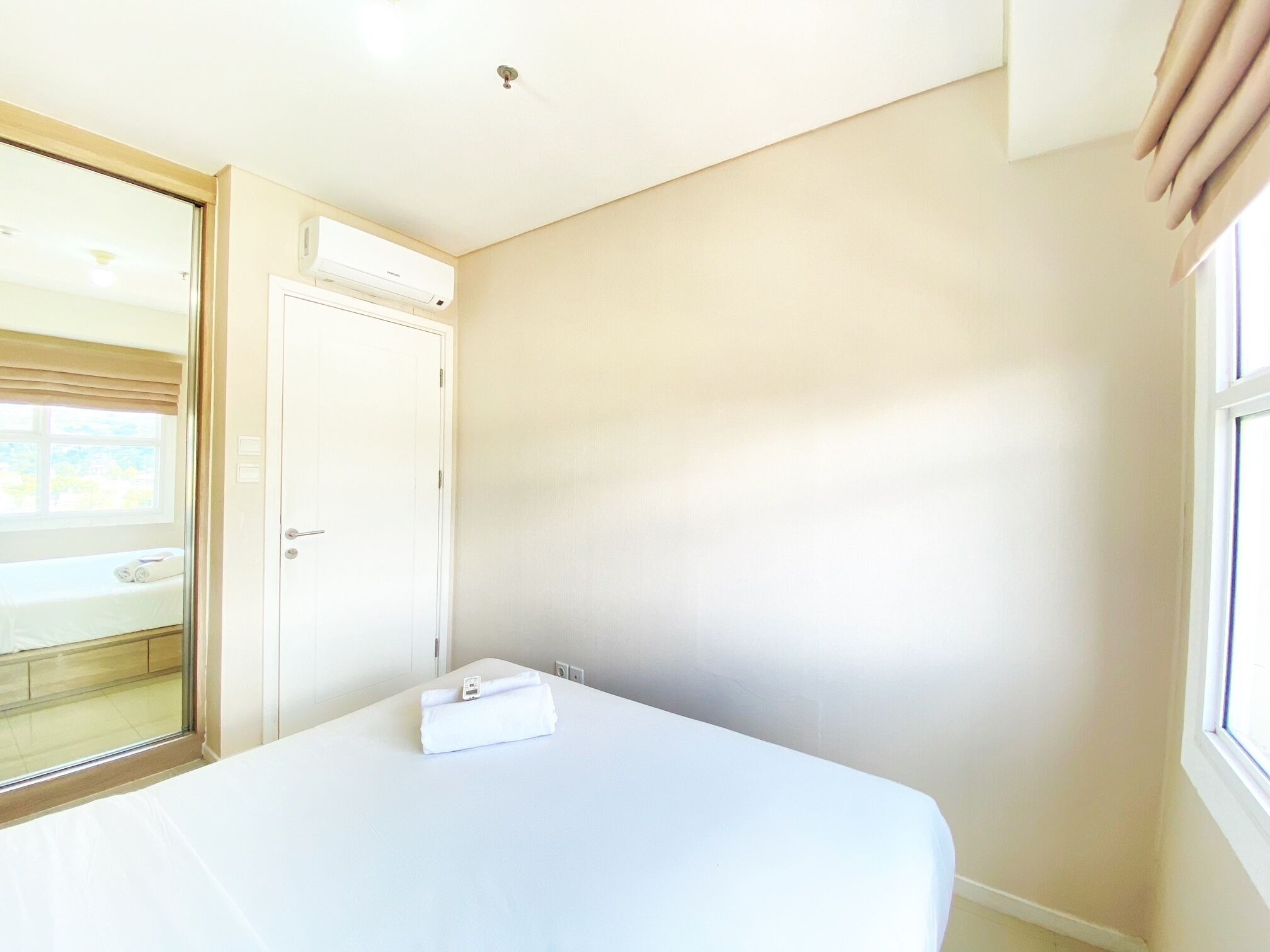 A hotel room with a bed, a window, a door, and an air conditioning unit.