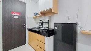 Una cocina compacta con una puerta de madera oscura, un refrigerador negro, una encimera con un lavamanos y un armario de madera.