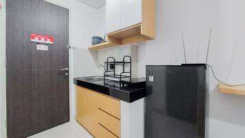 A compact kitchen with a dark wooden door, a black refrigerator, a countertop with a sink, and a wooden cabinet.