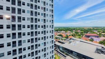 A high-rise building with a grid of windows and balconies, and a view of a town with various buildings and greenery.