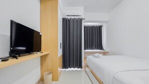 Una habitación de hotel moderna con una televisión de pantalla plana sobre una estantería de madera, una cama con ropa blanca y una mesita de noche.